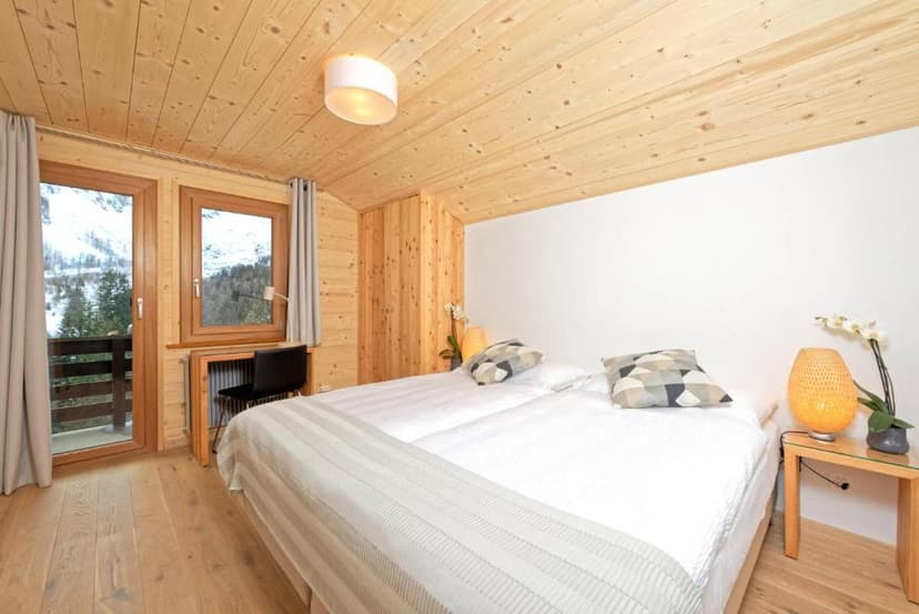 Bedroom with wood paneling and balcony view of snowy mountains in winter