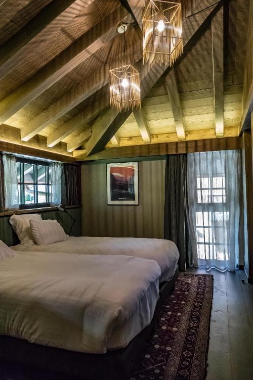 Twin beds in rustic room with exposed wood beams and geometric pendant lights, Hotel Hameau Albert 1er