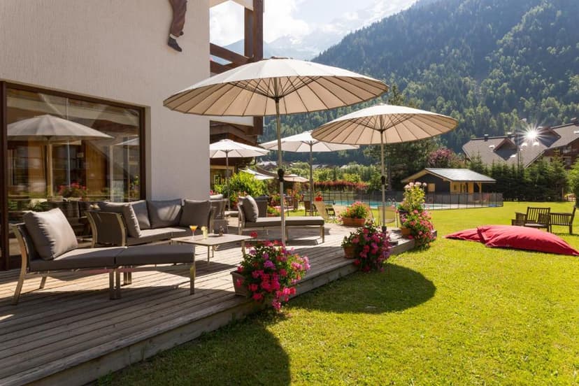 Outdoor lounge area with umbrellas on a wooden deck overlooking a grassy yard and mountains.
