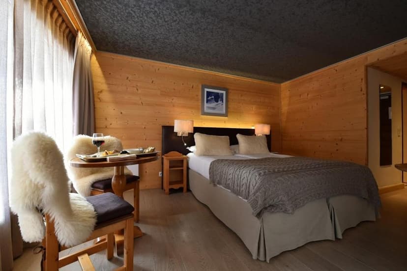 Cozy hotel room with wood paneling, twin beds, and a small table with wine and snacks.