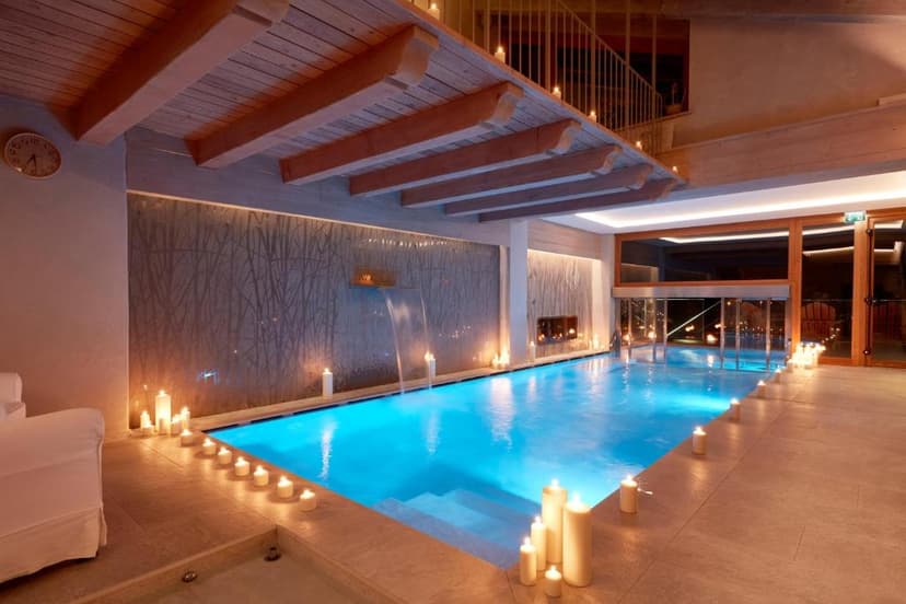 Indoor swimming pool illuminated by candlelight with a small waterfall feature and wood ceiling.