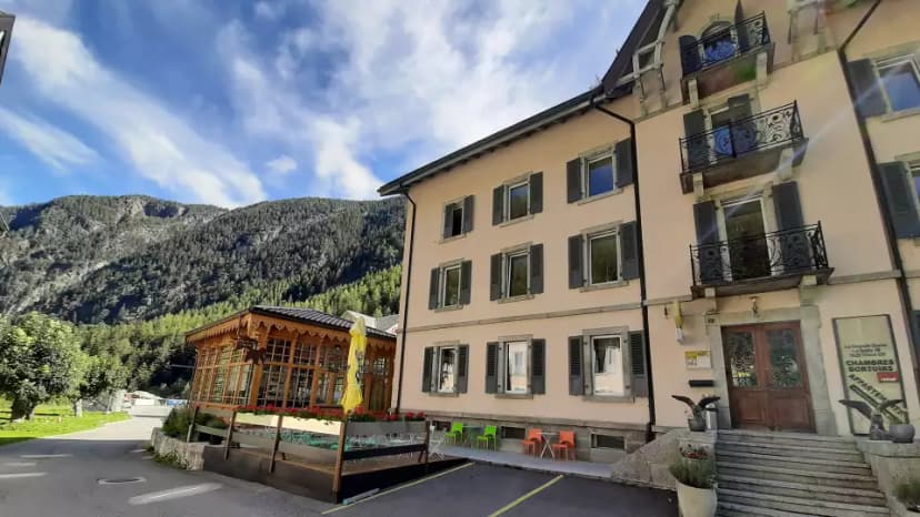 Alpine building with balconies next to a forested mountain under a blue sky in Trient.