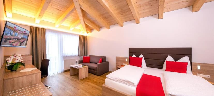 Hotel room with wooden beamed ceiling, modern bed with red accents, and a sofa.