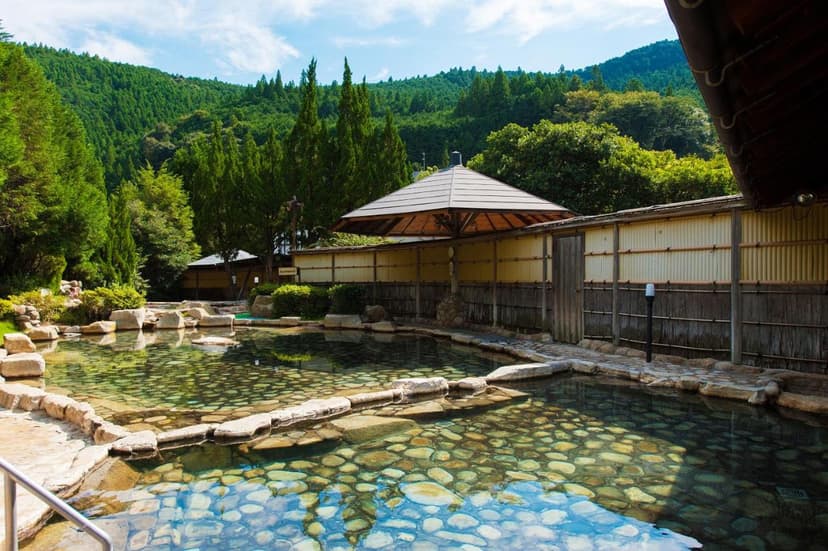 Outdoor onsen pool with clear water over stones at Watarase Onsen Hotel Sasayuri, surrounded by forest.