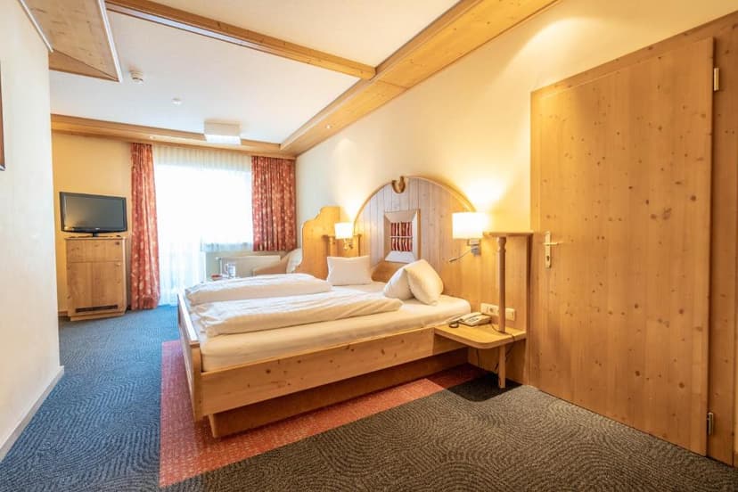 Hotel bedroom with wooden furniture, white bedding, and patterned carpet.