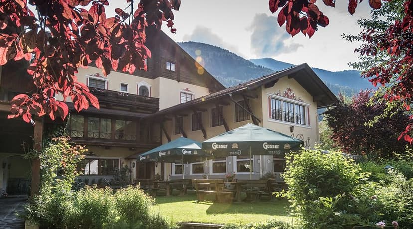 Alpine hotel exterior with outdoor seating under green umbrellas and mountain backdrop.