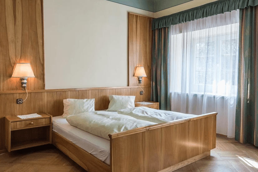 Double bed with wooden frame, white linens, and bedside lamps next to a bright window.