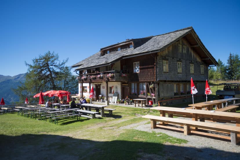 Alpengasthaus Marterle with outdoor seating and mountain backdrop under a clear blue sky.