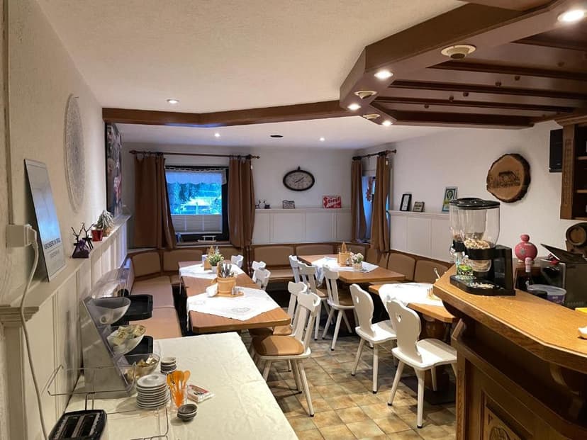 Dining area with wooden tables, white chairs, and a breakfast buffet setup.