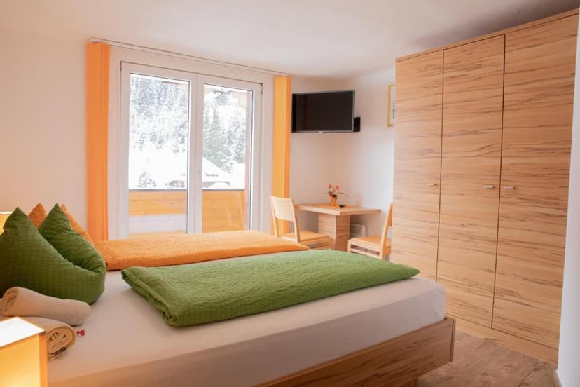 Hotel room with green and orange bedding, wooden furniture, and snowy view outside.