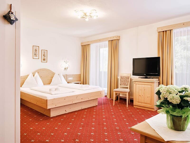 Bright hotel room with wooden furniture, twin beds, red patterned carpet, and flowers, Hotel Blattlhof.