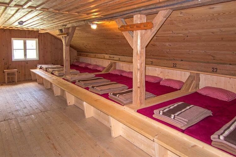 Bunk room with wooden berths, red mattresses, and blankets inside the Gruttenhütte mountain hut.