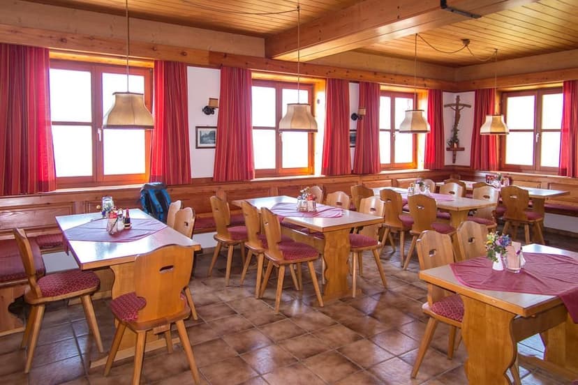 Rustic dining room with wooden tables and chairs, red curtains, and bright windows at Gruttenhütte.