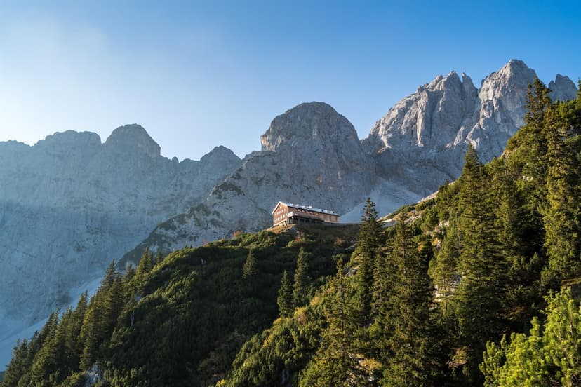 Gruttenhütte mountain hut nestled on a slope below rugged limestone peaks with evergreen trees.