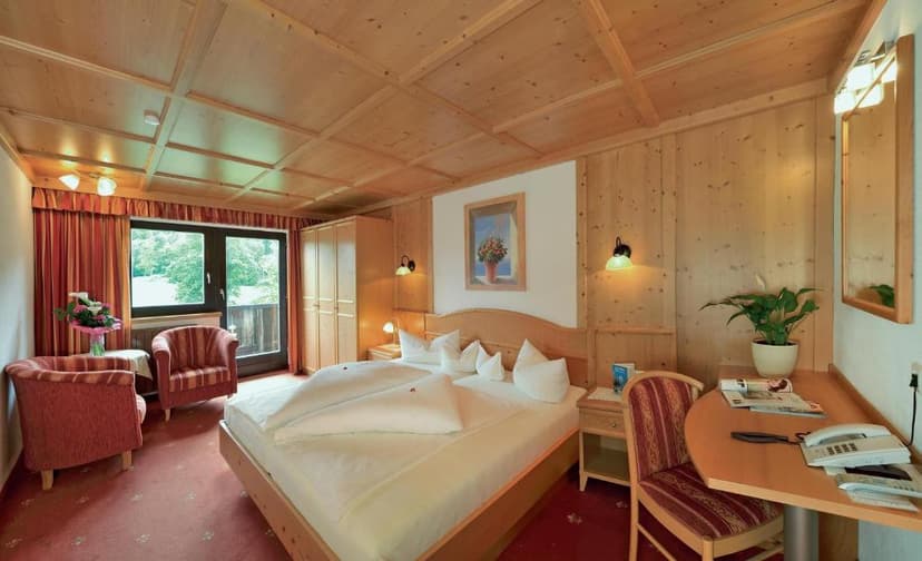Hotel room with wood paneling, double bed, seating area, and view of greenery through balcony doors.