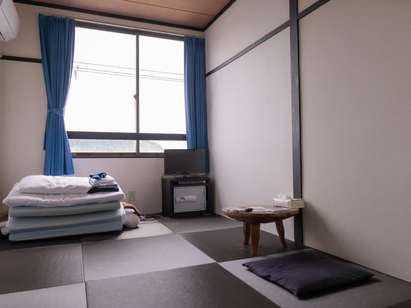 Japanese-style room with futon bedding, low wooden table, and television near a window with blue curtains.