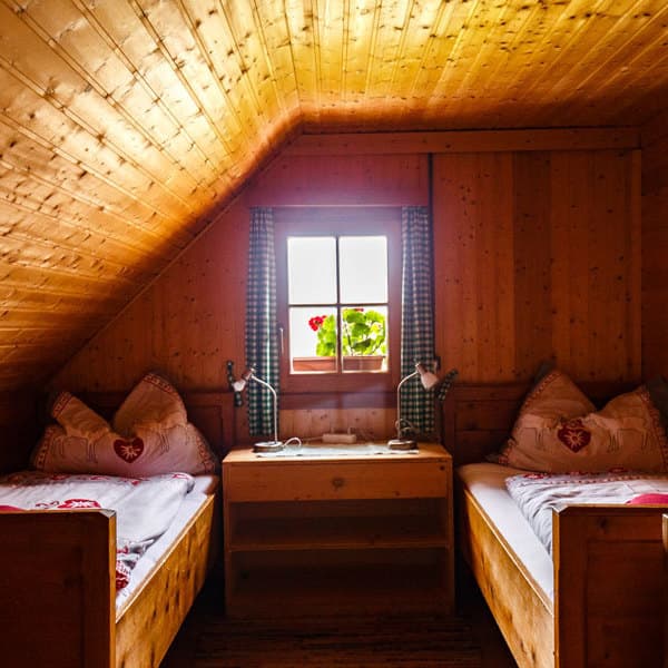 Rustic wooden attic bedroom with twin beds, small window, and geraniums at Millstätter Hütte.