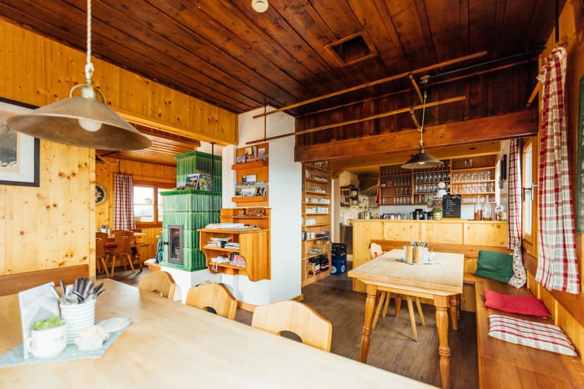 Interior of Goisererhütte with wood paneling, green tiled stove, and dining area.