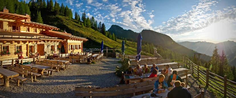 Loosbühelalm mountain hut with outdoor dining terrace overlooking sunlit alpine valley.