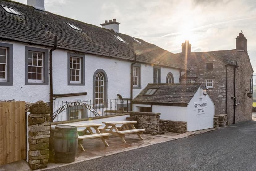 The Greyhound Hotel exterior with picnic tables, barrel, and sun flare over slate roof.