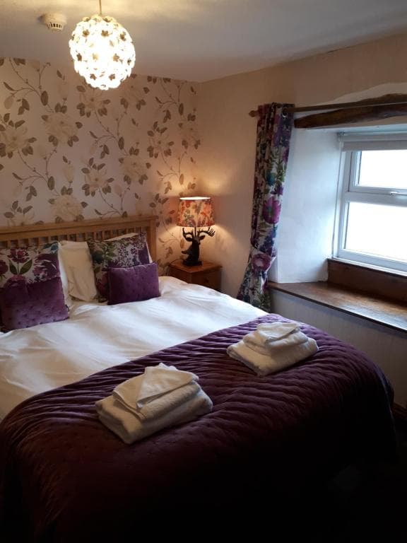Bedroom with floral wallpaper, purple quilt, and towels stacked on the bed at The Black Bull at Nateby.