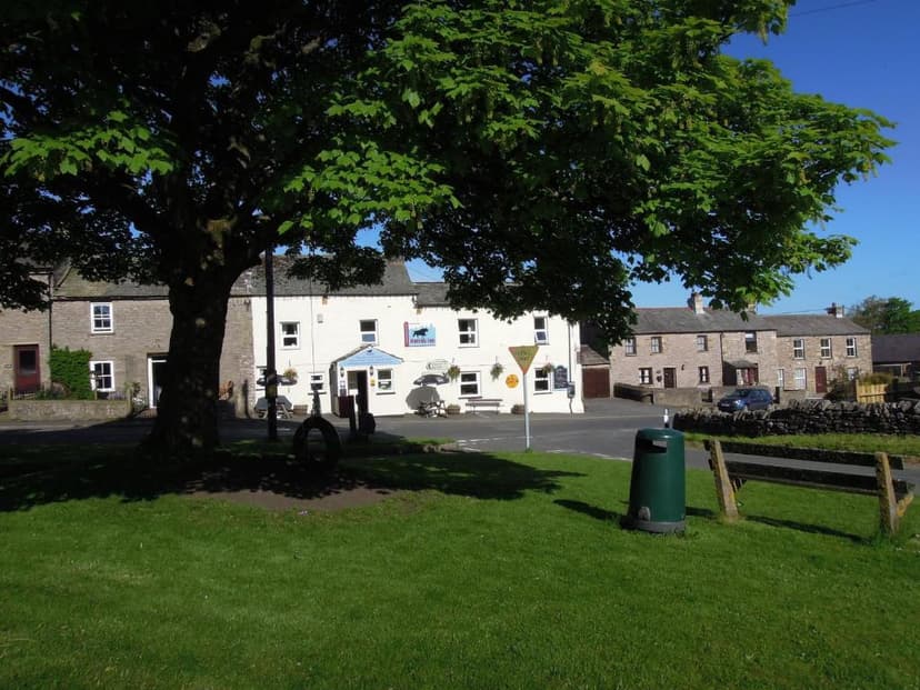 White pub with sign under large tree in village square, Nateby, UK