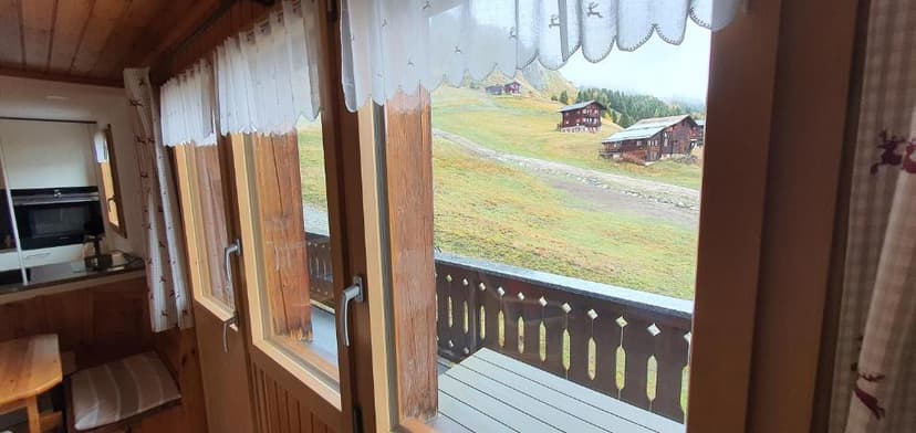 View from wooden balcony toward alpine chalets on grassy hillside in Riederalp.