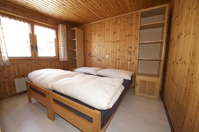 Wooden bedroom with pine paneling, white bedding, and built-in shelving in Riederalp.