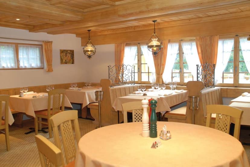 Restaurant dining room with wood paneling, set tables, and bright windows overlooking greenery.