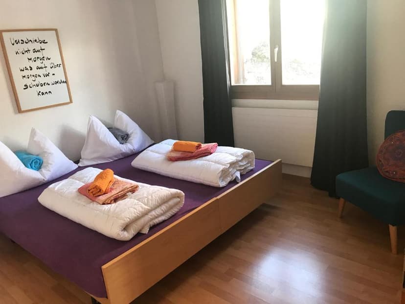 Bedroom with wooden floor, twin beds, white bedding, and German writing on a whiteboard.