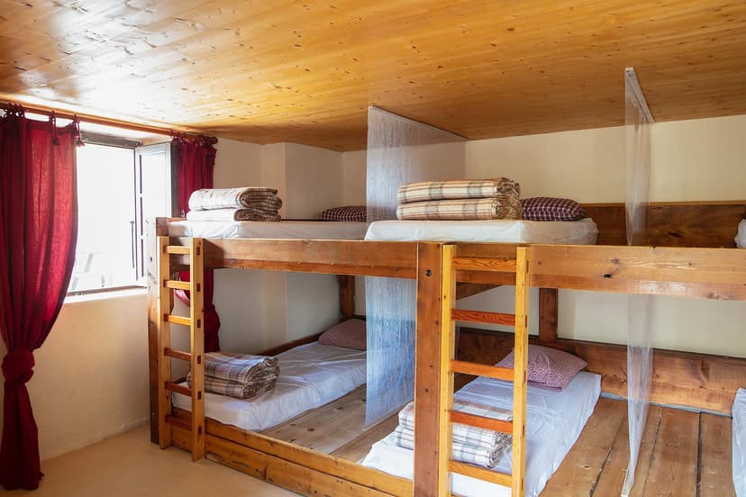 Wooden bunk beds with blankets and pillows inside a room with a wooden ceiling at Refuge Col de Balme.
