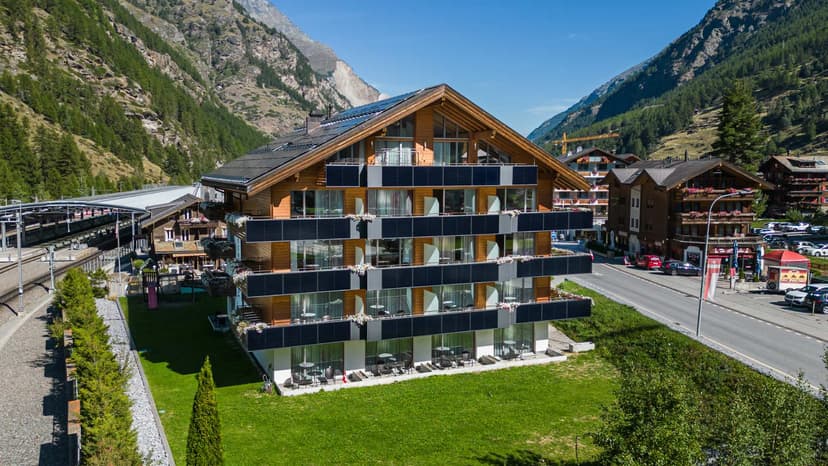 Hotel Taescherhof building with balconies, green lawn, and steep forested mountains.