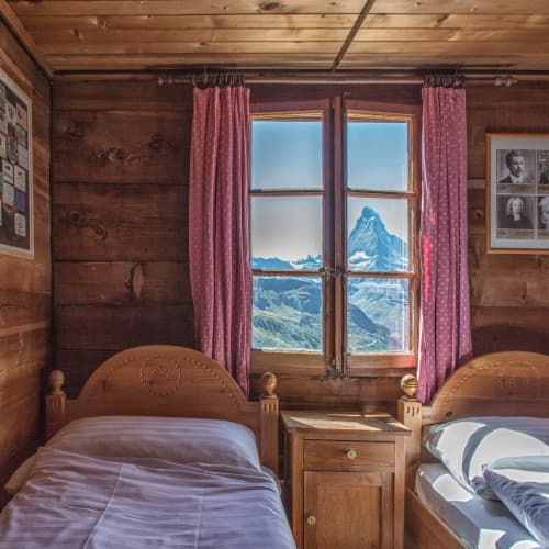 Hut interior with wooden walls, beds, and window view of the Matterhorn peak.