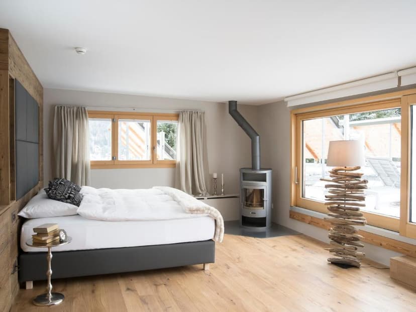 Bedroom with wood stove, white bedding, and driftwood floor lamp in Davos hotel