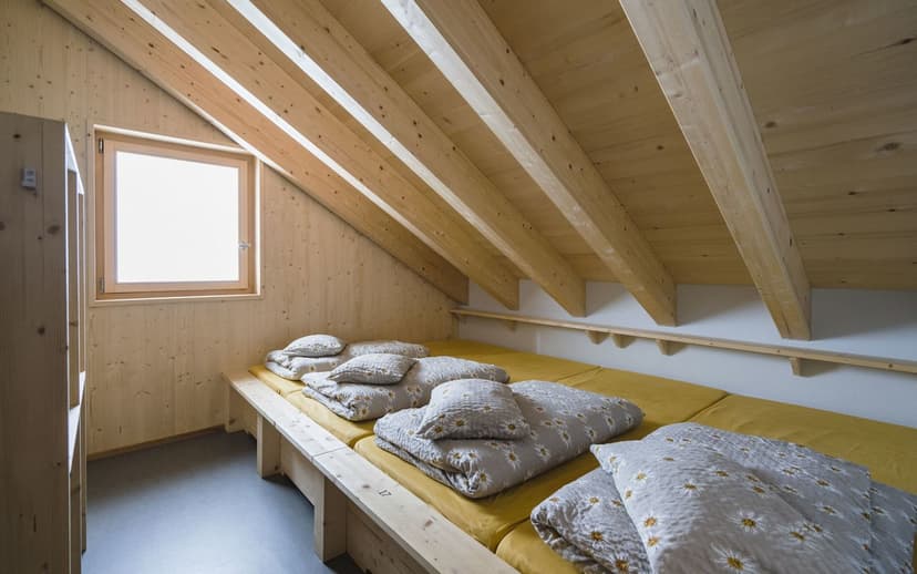 Bunk room in Grialetsch Hut with wood paneling, sloped ceiling, and daisy-patterned bedding.