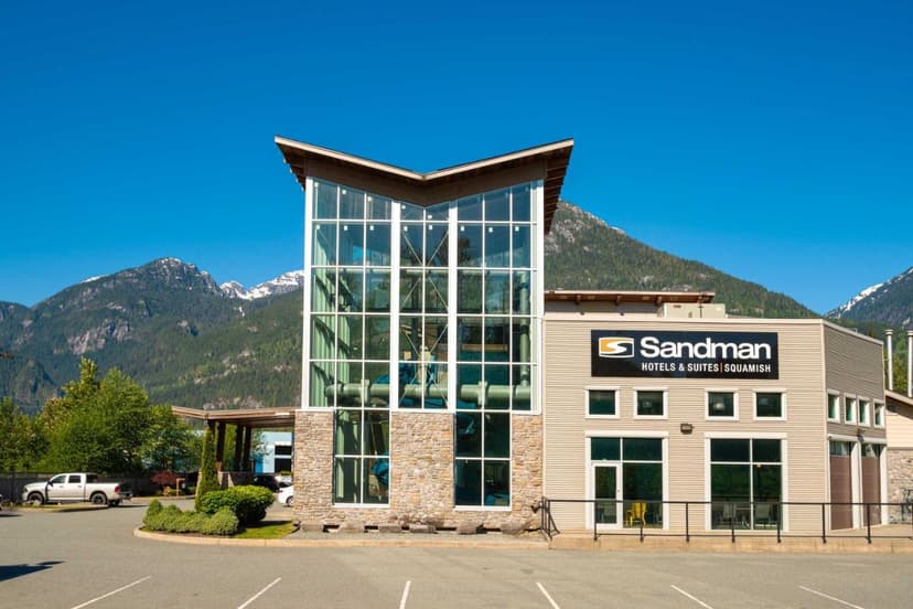 Sandman Hotels & Suites Squamish building with glass facade against mountains under blue sky.