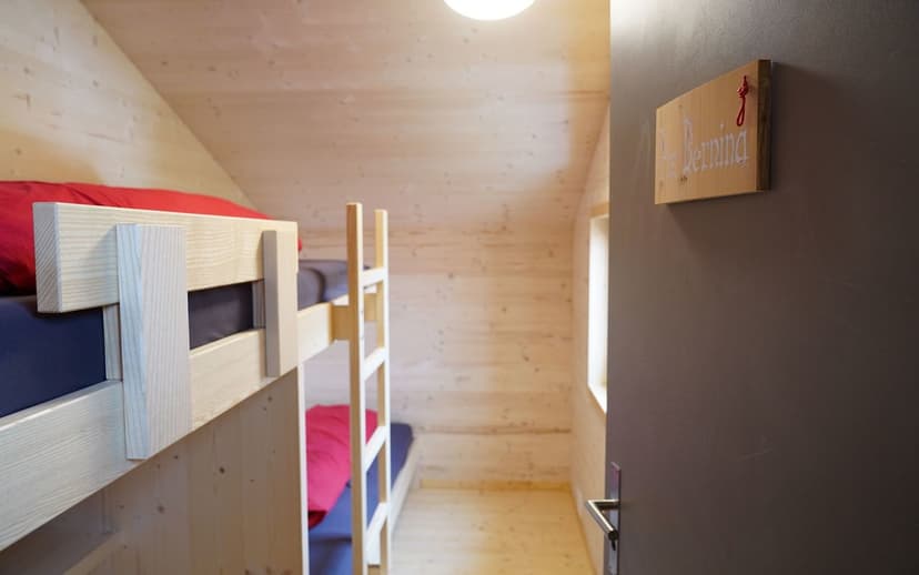 Bunk beds in wood-paneled attic room with a "Bernina" sign on the dark door.