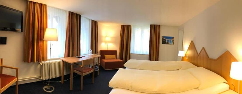 Hotel Weisses Kreuz guest room with large bed, desk, chair, and bright windows.