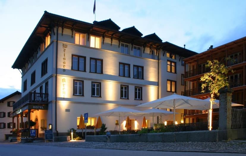 Hotel Weisses Kreuz building illuminated at dusk with outdoor patio seating and umbrellas.