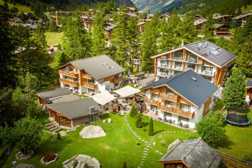 Hotel Hemizeus buildings with green lawn, outdoor dining area, and surrounding alpine village.