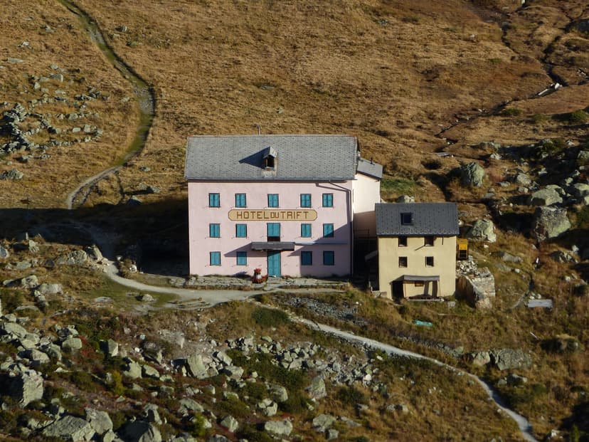 Hotel du Trift building nestled in a rocky, grassy mountainside with hiking paths.