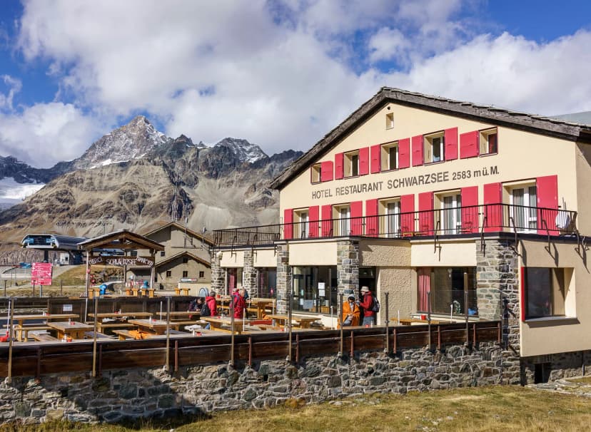Hotel Restaurant Schwarzsee at 2583m with outdoor seating and snow-capped mountains.