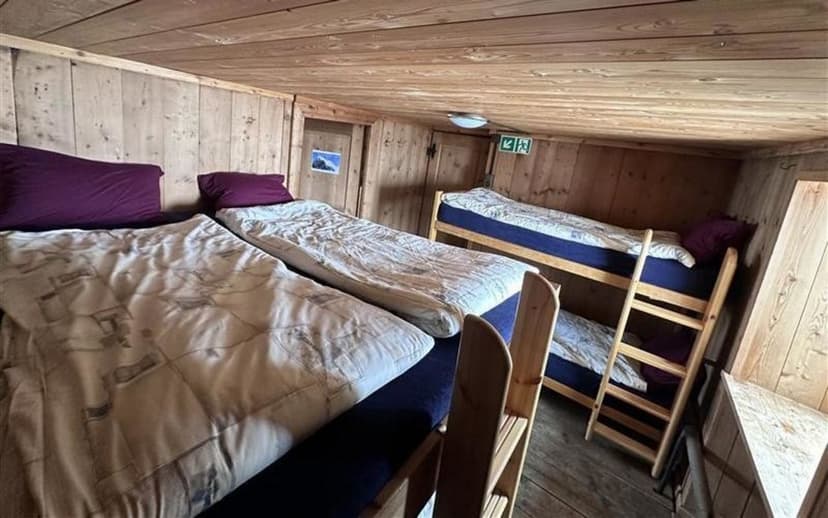 Bunk beds and single beds in a rustic wooden room, likely a mountain hut or hostel.