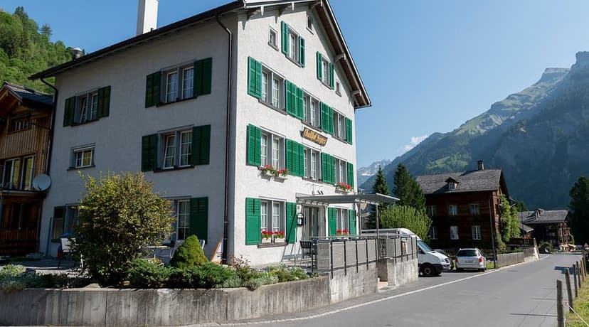 Hotel Segnes building with green shutters in an alpine village setting with mountains.