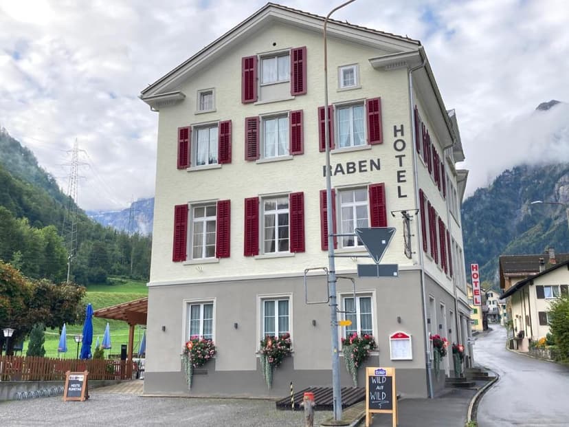 Hotel Raben building with red shutters in a mountain valley setting under cloudy skies