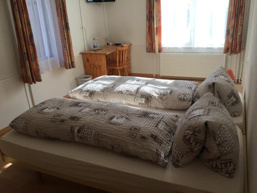 Twin beds with patterned duvets and pillows in a bright room with a wooden desk.