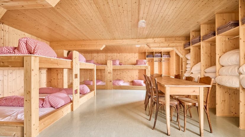 Wooden dormitory room with bunk beds, dining table, and storage shelves at Hotel Klausenpass.