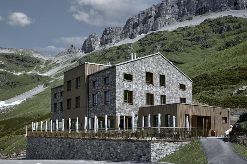 Hotel Klausenpass stone building with outdoor terrace set against steep green alpine mountains.