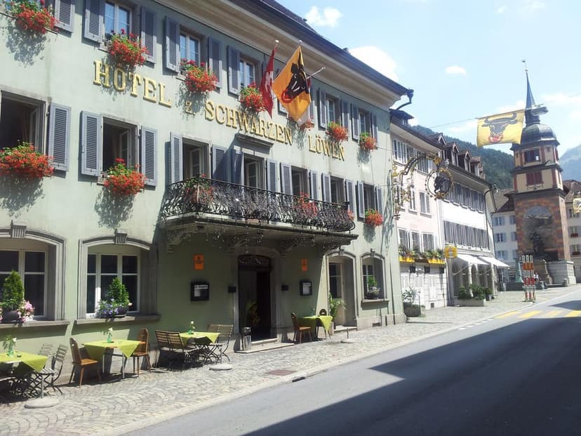Hotel zum Schwarzen Löwen with outdoor cafe seating on cobblestone street near a clock tower.