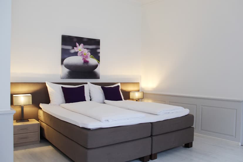 Hotel room with twin beds, white linens, purple pillows, and spa stone artwork.